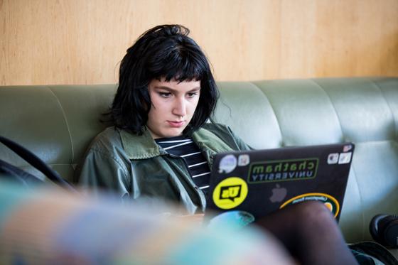 图为一位波胆网站的女学生坐在图书馆的沙发上, working on her laptop